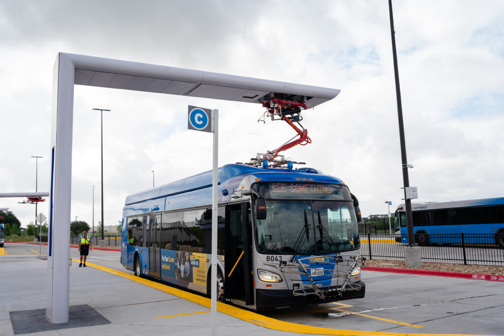 Electric bus at a stop and connected to a charging hub.
