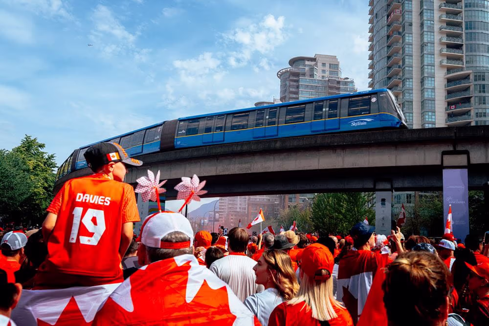 A SkyTrain passes by crowds outside Main Street–Science World Station before the Canada/Switzerland Match.