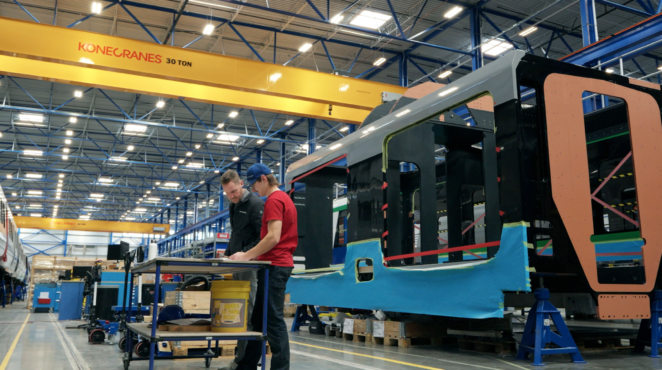 Two people working in front of a light rail vehicle being put together in a manufacturing facility.
