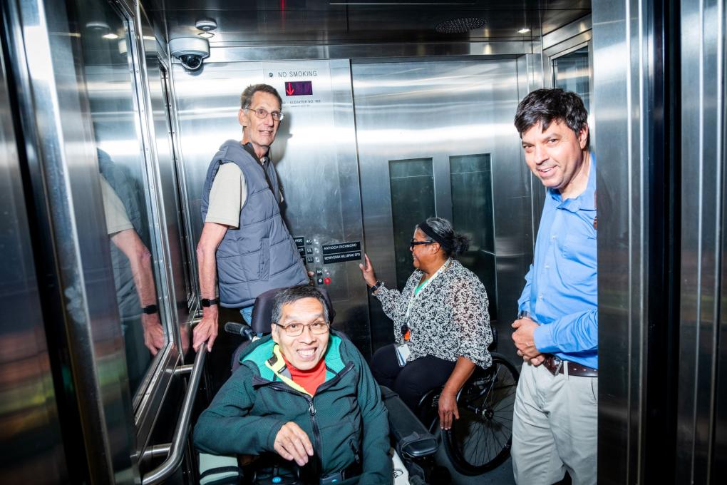 Four people, two of whom are using a wheelchair, in an elevator. 