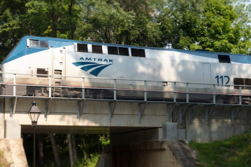 Amtrak train going over a bridge with green leafy trees in the background.