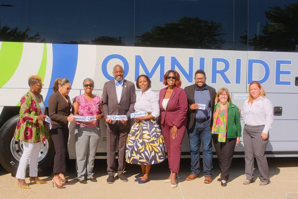 Representatives pose in front of an Omniride bus
