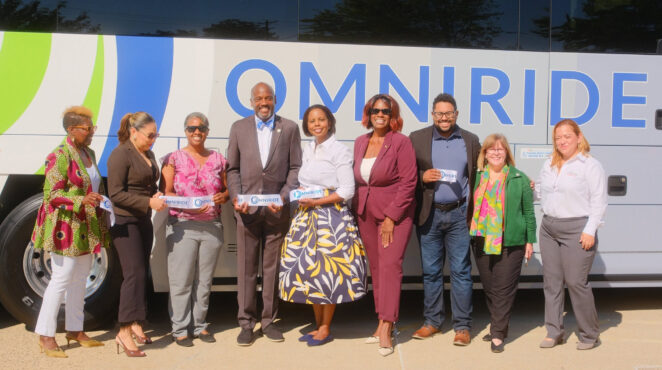 Representatives pose in front of an Omniride bus