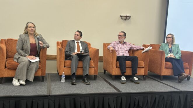 Four conference speakers seated on stage.