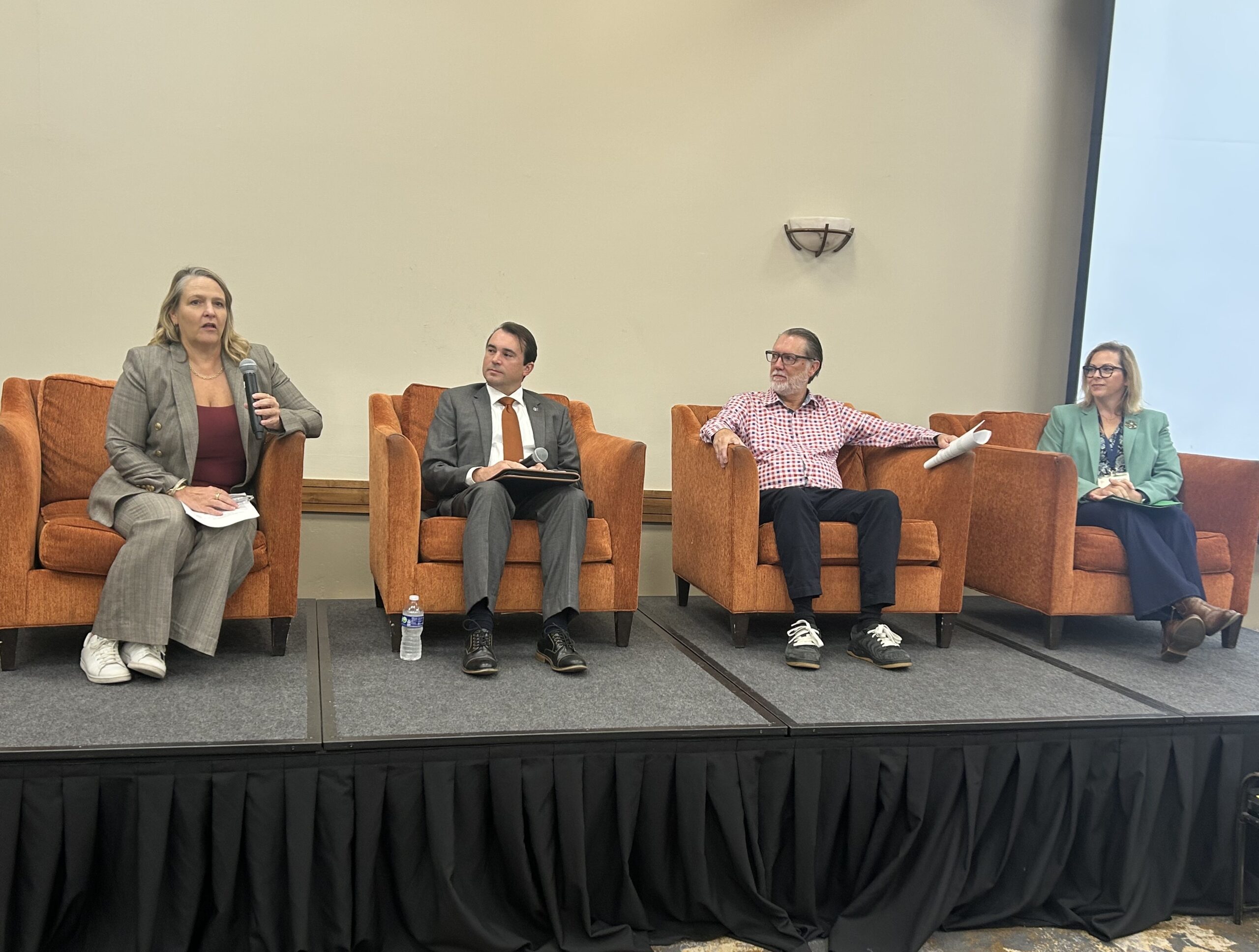 Four conference speakers seated on stage.