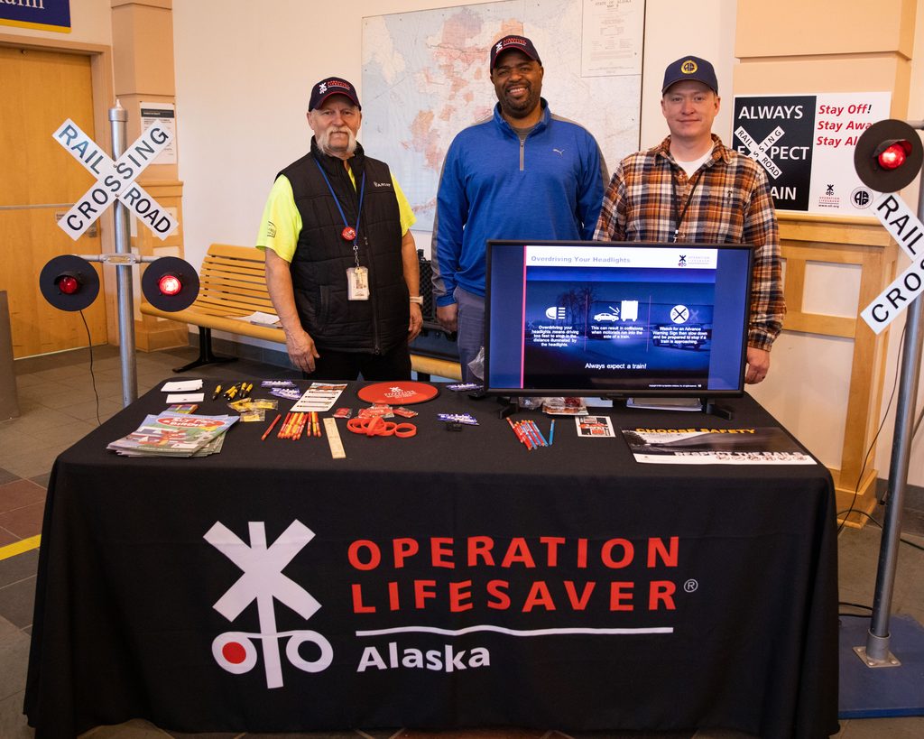 Three people pose at a table with Operation Lifesaver Alaska materials.